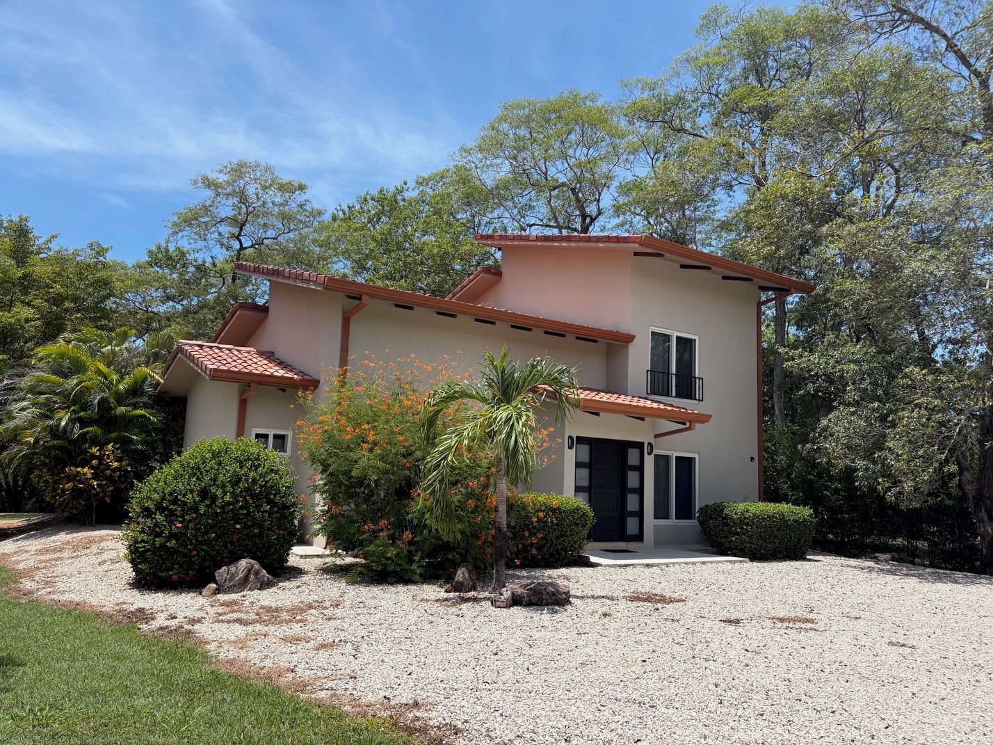 A two-story house with a gravel driveway, surrounded by greenery and trees.