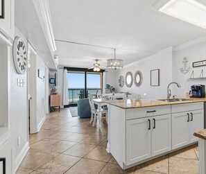 A modern kitchen with a large island, white cabinetry, and a view to the outside. - A Little Peace of the Beach (Orange Beach)