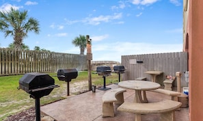 Een buitenpatio met een ronde tafel en bankjes, omgeven door een houten omheining en een palmbom.