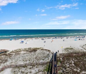 Ein Strand mit einer Holzpromenade, die zum Ufer führt, feinem Sand und blauem Himmel.