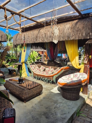 A thatched-roof outdoor seating area with wicker furniture and a chessboard.