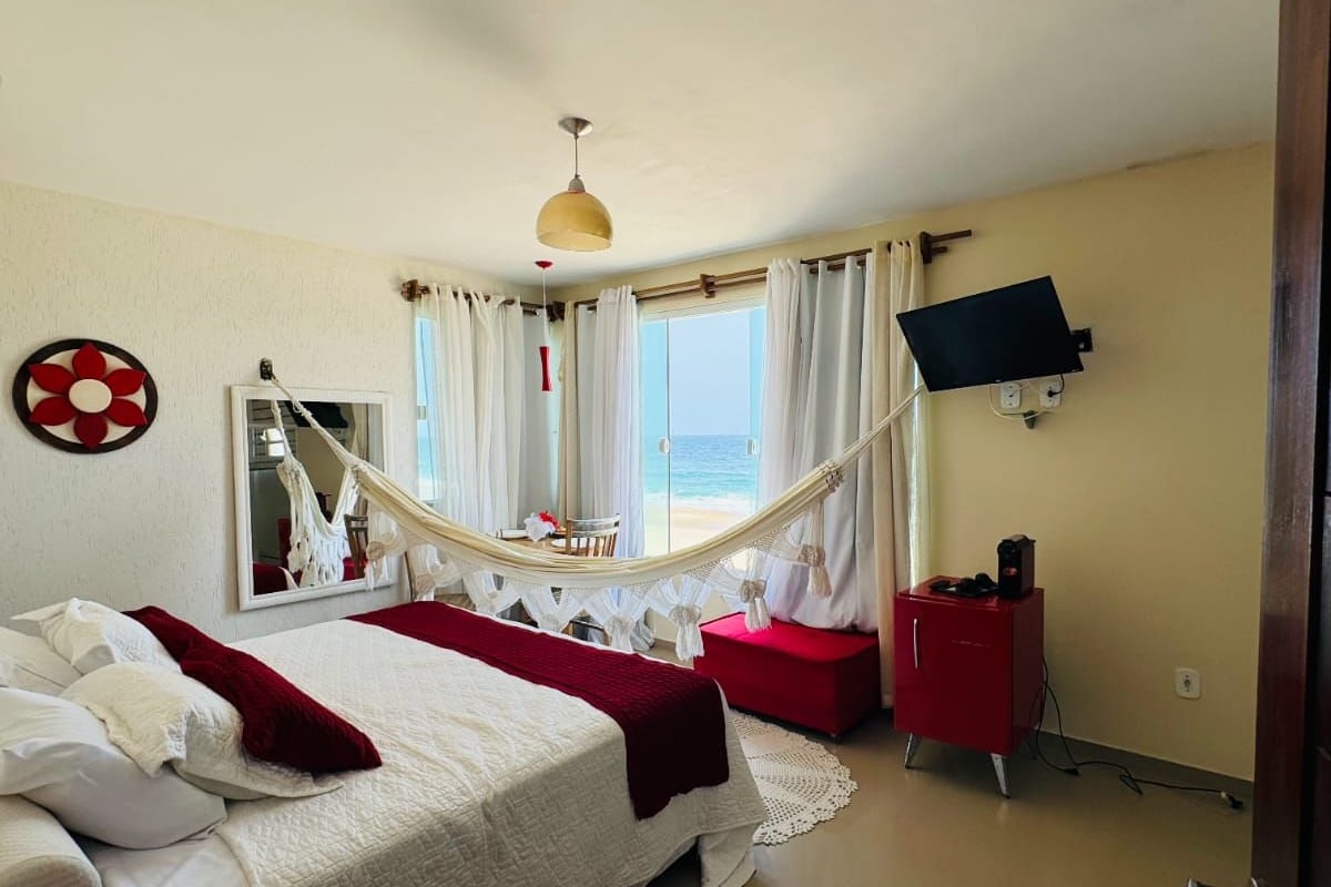 Ett hotellrum med en säng, ett rött skåp, en tv som är monterad på väggen och utsikt över havet genom fönstret.