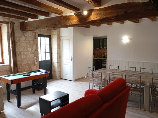 Une pièce comprenant une table de billard, une table à manger avec des chaises, un canapé rouge et un coin cuisine.