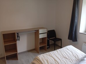 Une chambre à coucher avec un lit, un bureau avec une chaise et une fenêtre avec des rideaux.