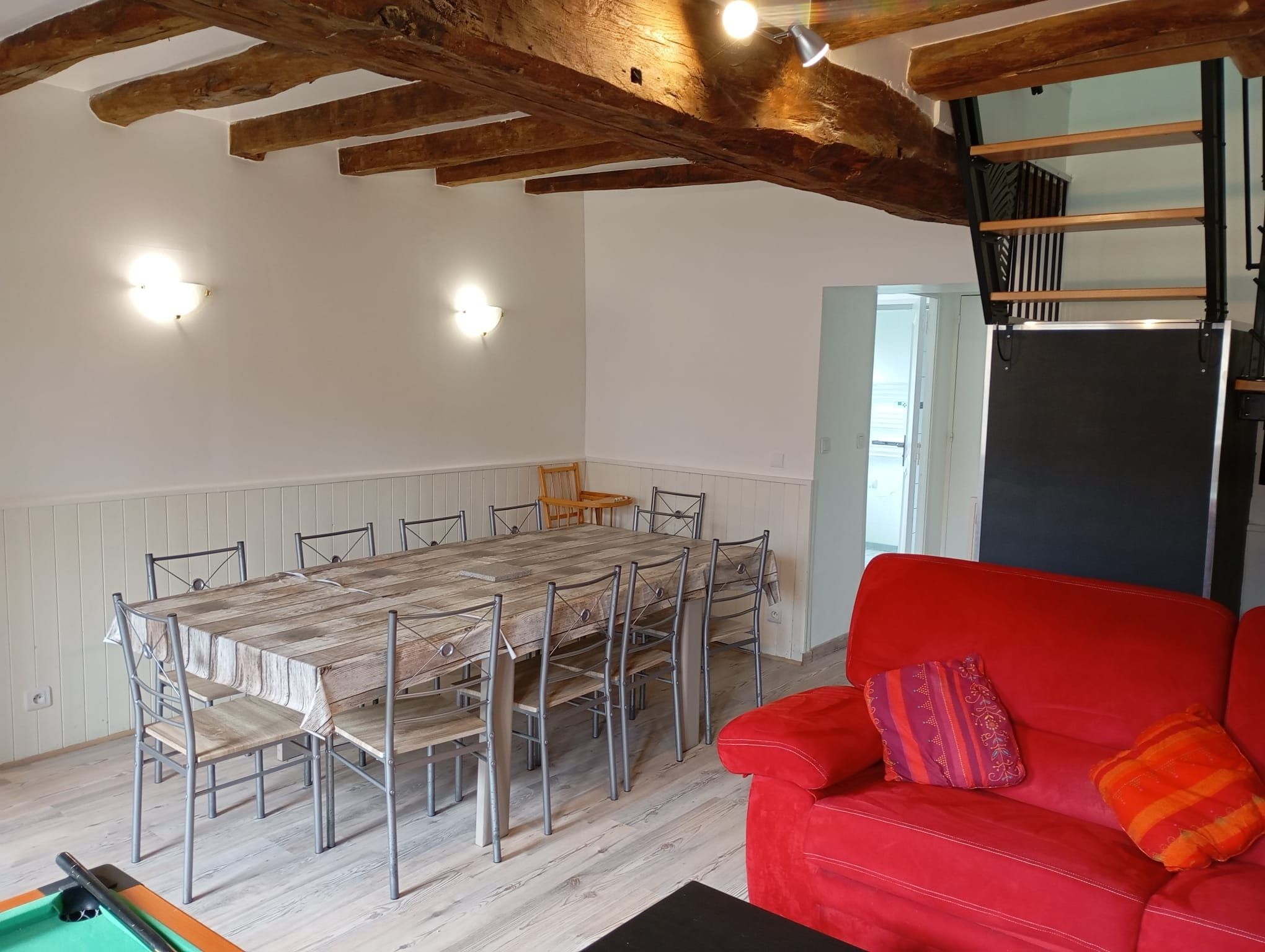 A dining area with a wooden table and chairs, a red sofa, and a billiards table.