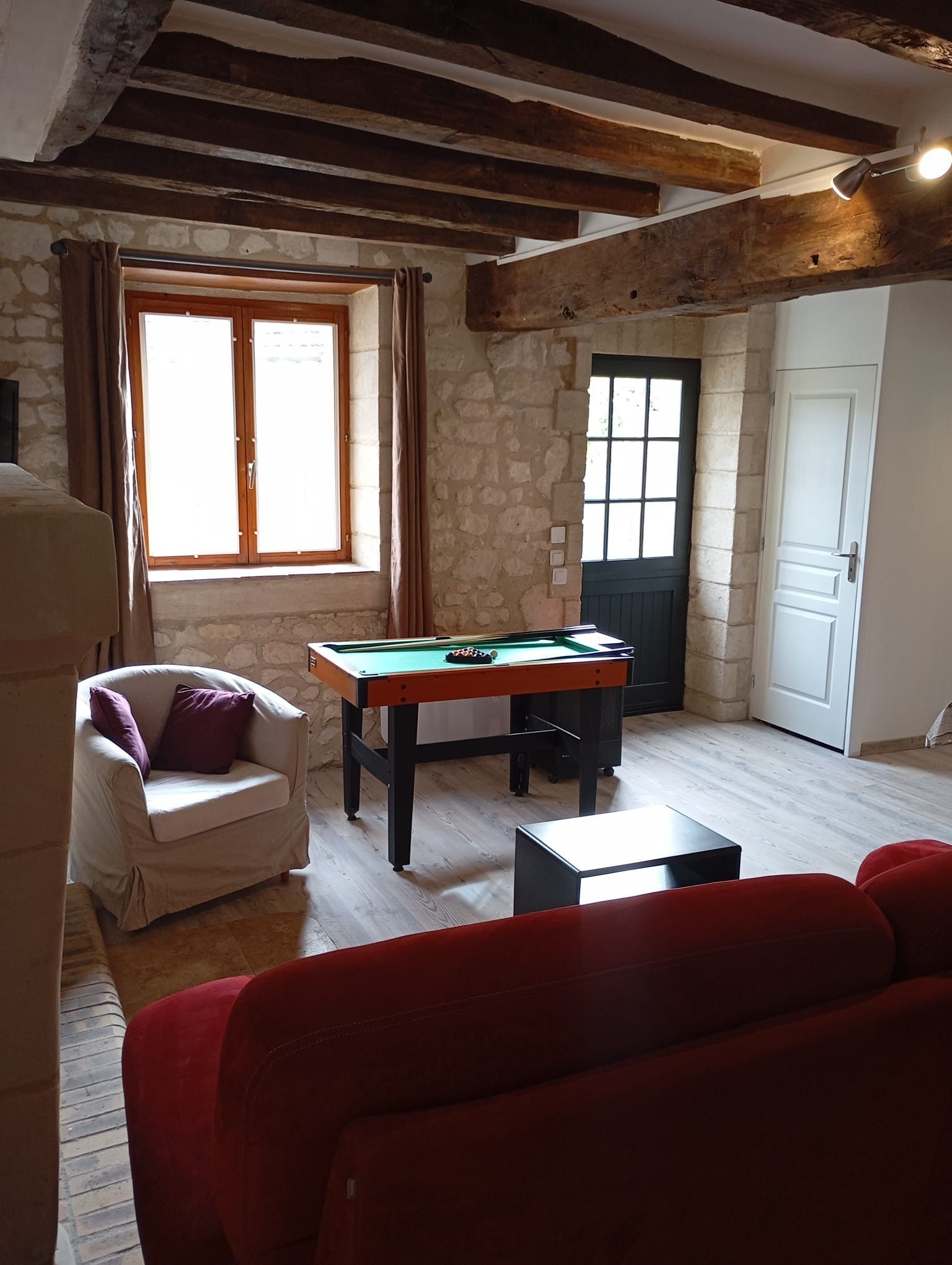 A room with a pool table, a white armchair, and a red sofa.