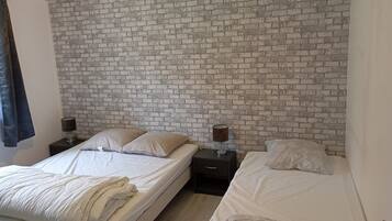 A bedroom with two beds, a brick-patterned headboard, bedside lamps, and a window with curtains.