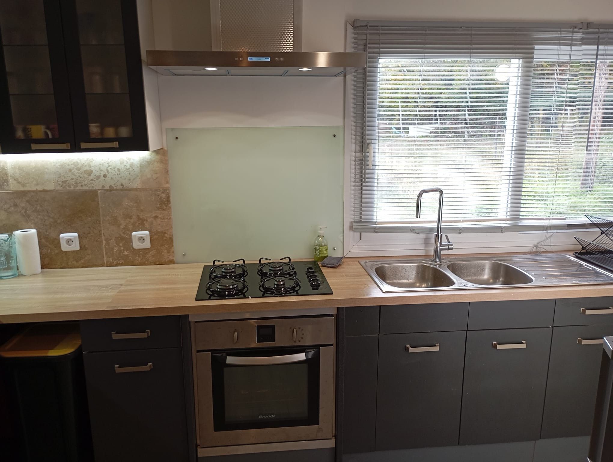 A modern kitchen with a gas stove, oven, double sink, and a window with blinds.