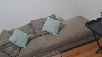 Una habitación con un sofá junto a una pared, una pequeña mesa con un jarrón y suelo de madera.