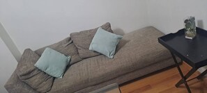 Una habitación con un sofá junto a una pared, una pequeña mesa con un jarrón y suelo de madera.
