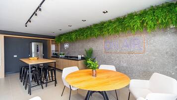 Une cuisine moderne équipée d’un réfrigérateur encastré, d’une table à manger en bois avec des chaises, et d’un néon mural indiquant « EN DIRECT ».