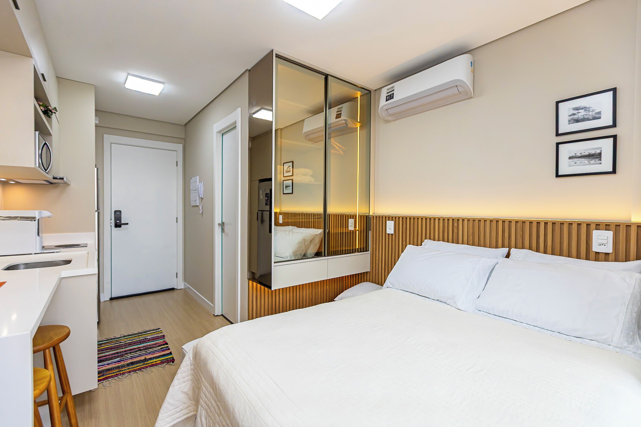 A hotel room with a bed, a mirror, an air conditioning unit, a desk, and a small bathroom.