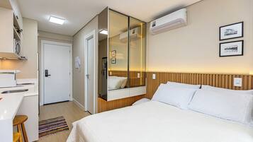 A hotel room with a bed, a mirror, an air conditioning unit, a desk, and a small bathroom.
