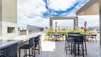 Een terras buiten met een bar, zitplaatsen en uitzicht op de skyline van de stad.