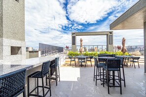 Una terraza al aire libre con zona de bar, asientos y vistas del horizonte de la ciudad.