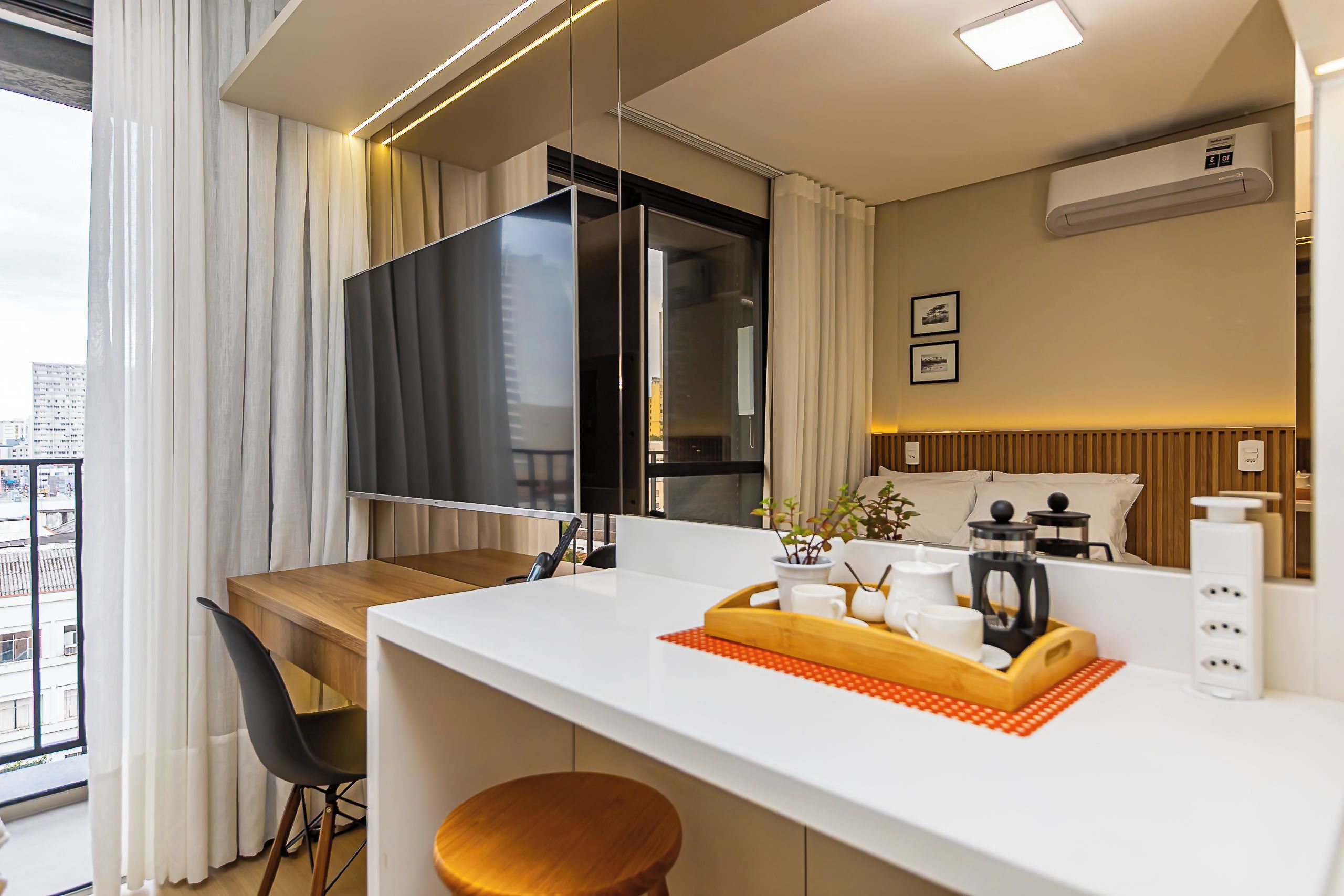 Une chambre d’hôtel moderne dotée d’un balcon, d’un téléviseur à écran plat, d’une table à manger en bois, d’un petit coin cuisine et offrant une vue sur le paysage urbain.