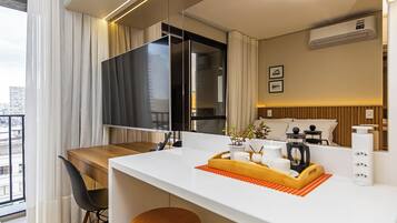 Une chambre d’hôtel moderne dotée d’un balcon, d’un téléviseur à écran plat, d’une table à manger en bois, d’un petit coin cuisine et offrant une vue sur le paysage urbain.
