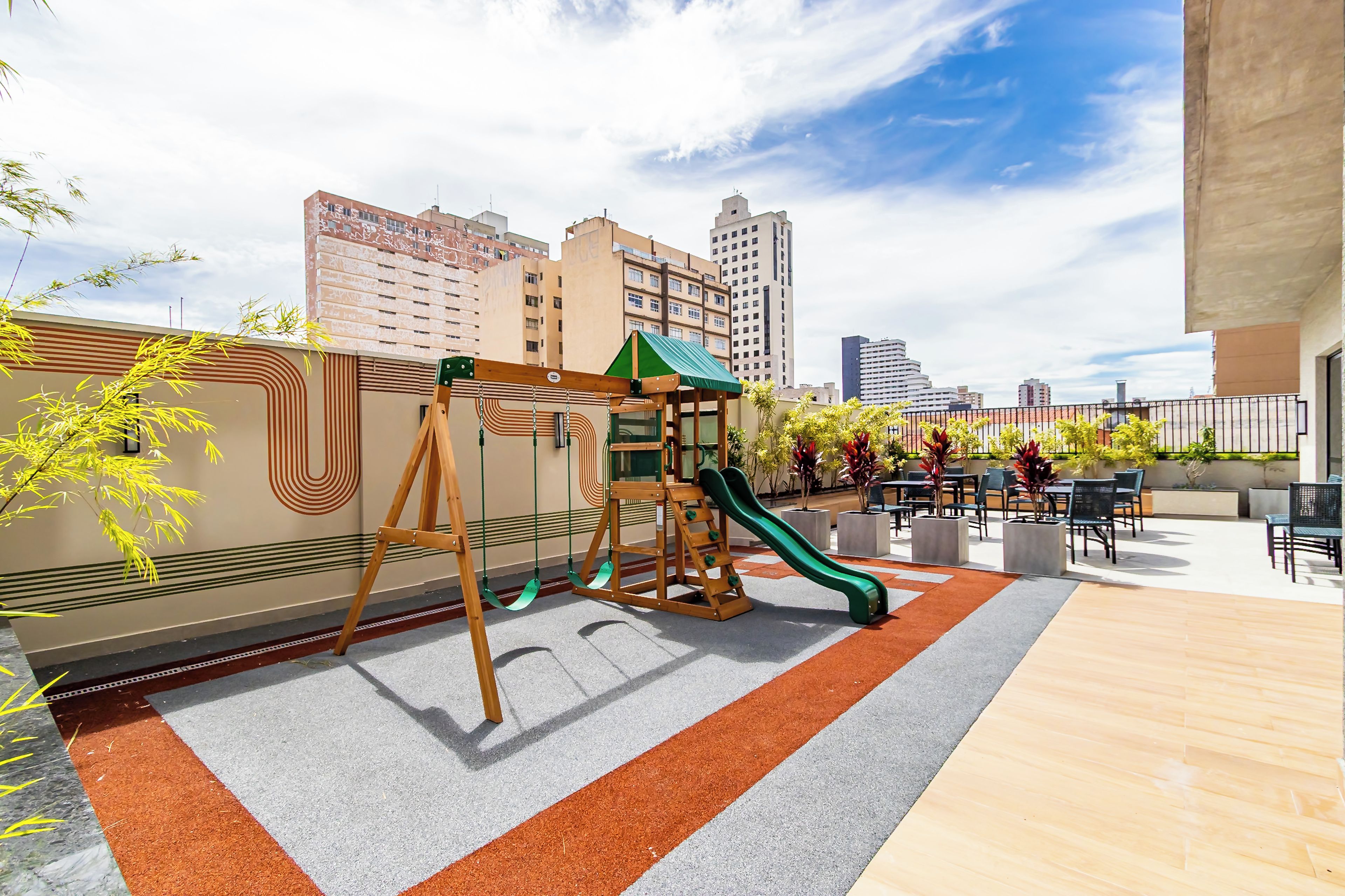 A rooftop playground with a slide and swings, surrounded by city buildings.