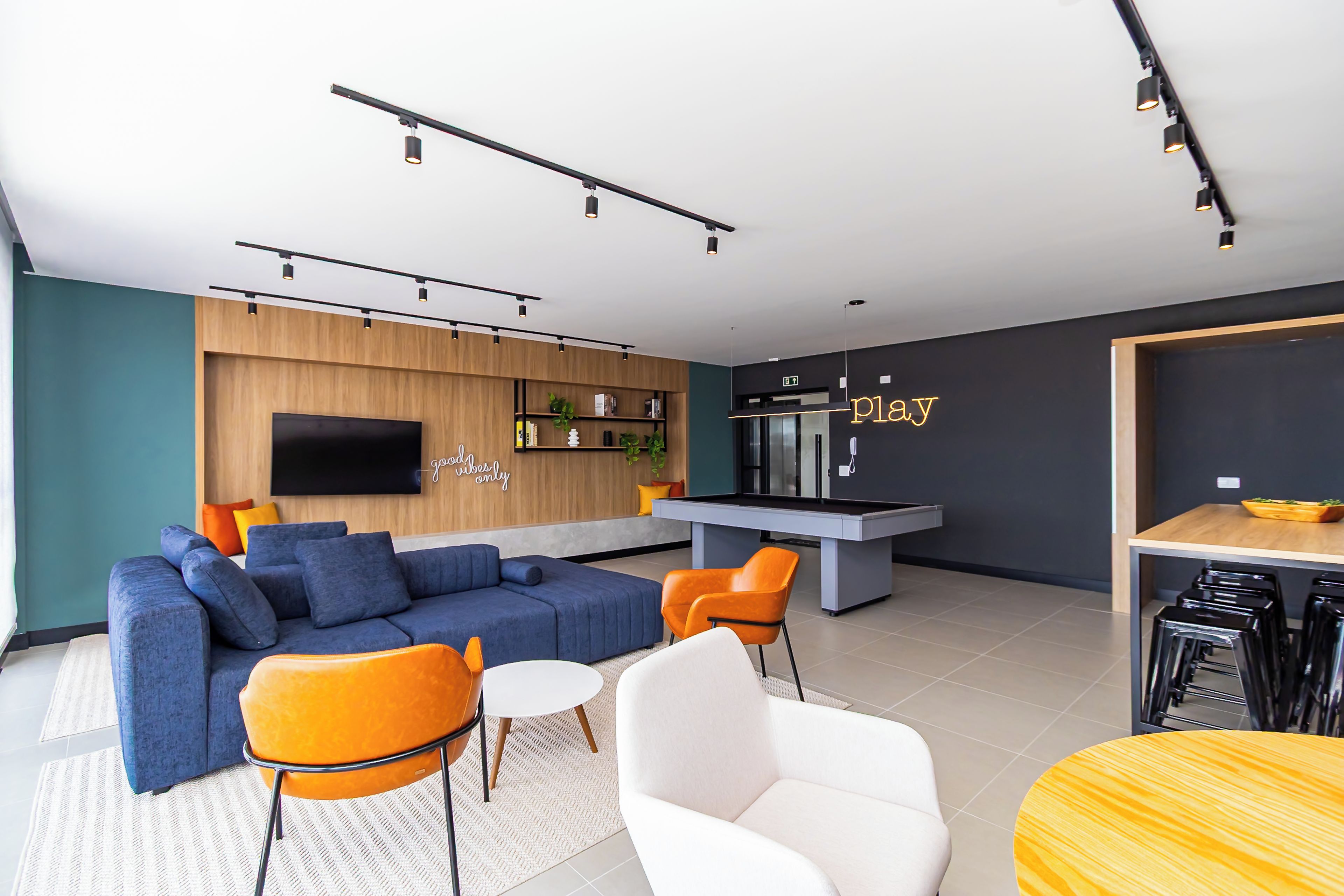 Un salon moderne comprenant un canapé, des fauteuils, un téléviseur, un coin cuisine et un bar.
