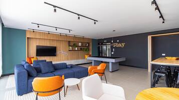 Un salon moderne comprenant un canapé, des fauteuils, un téléviseur, un coin cuisine et un bar.