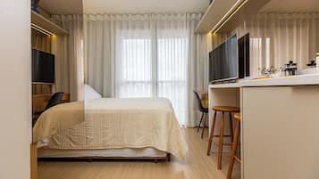 Ein Hotelzimmer mit einem Bett, einem Schreibtisch, einem Sessel, einem Fernseher und einem Fenster mit Vorhängen.