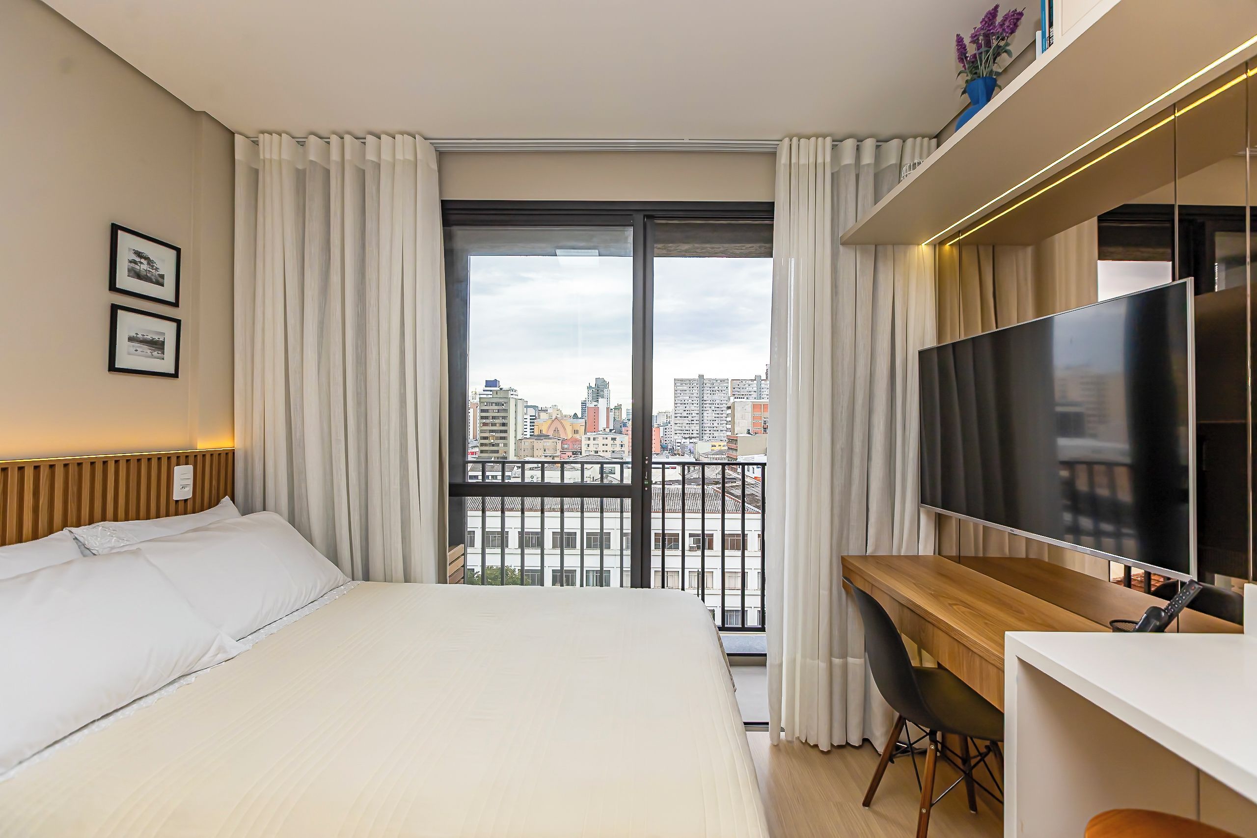 Una habitación de hotel con cama, escritorio, televisor y vistas a la ciudad.
