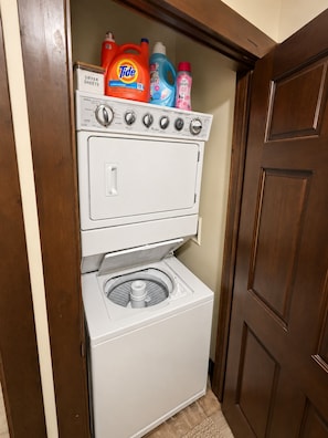 Máquina de lavar e secar compacta, com detergente Tide e outros produtos de limpeza por cima.