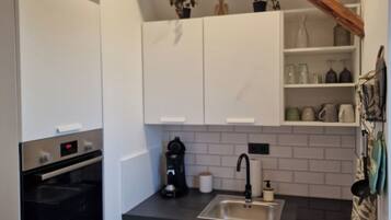 A compact kitchen with white upper cabinets, a black countertop, a built-in oven, a coffee maker, and a sink.