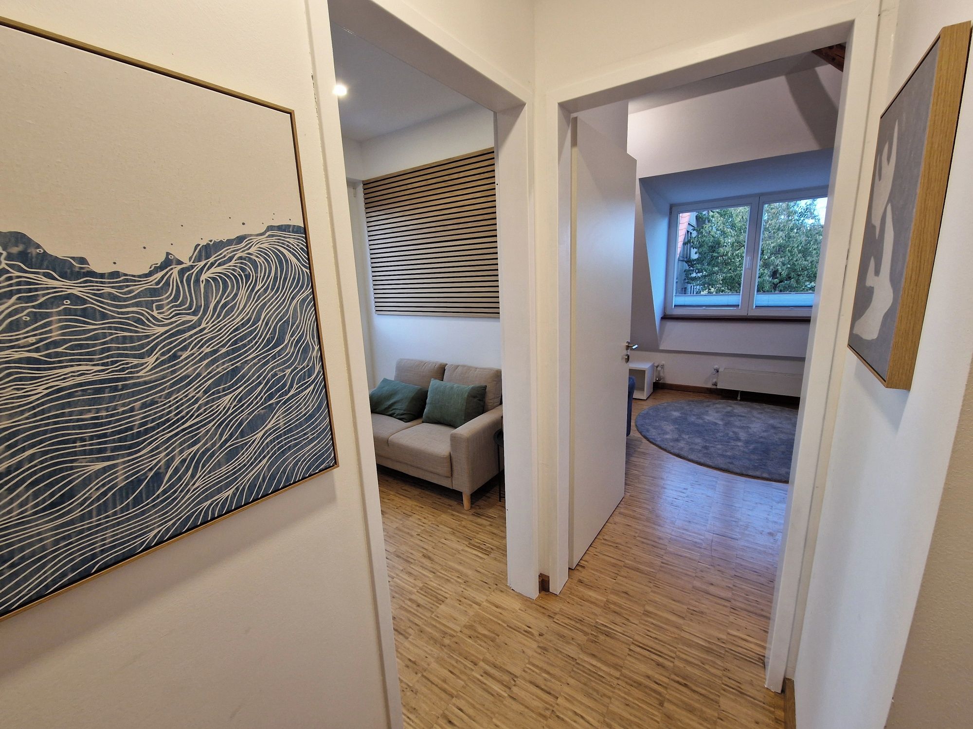 Un couloir doté d’un plancher en bois, d’un canapé avec des coussins et d’un grand tableau abstrait accroché au mur.