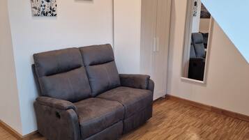 Ein Zimmer mit einem braunen Ledersofa, einem weißen Kleiderschrank und Holzboden.