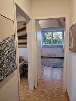 Ein Flur mit Holzboden, einem Fenster mit Jalousien, einem Heizkörper und einem grauen Teppich.
