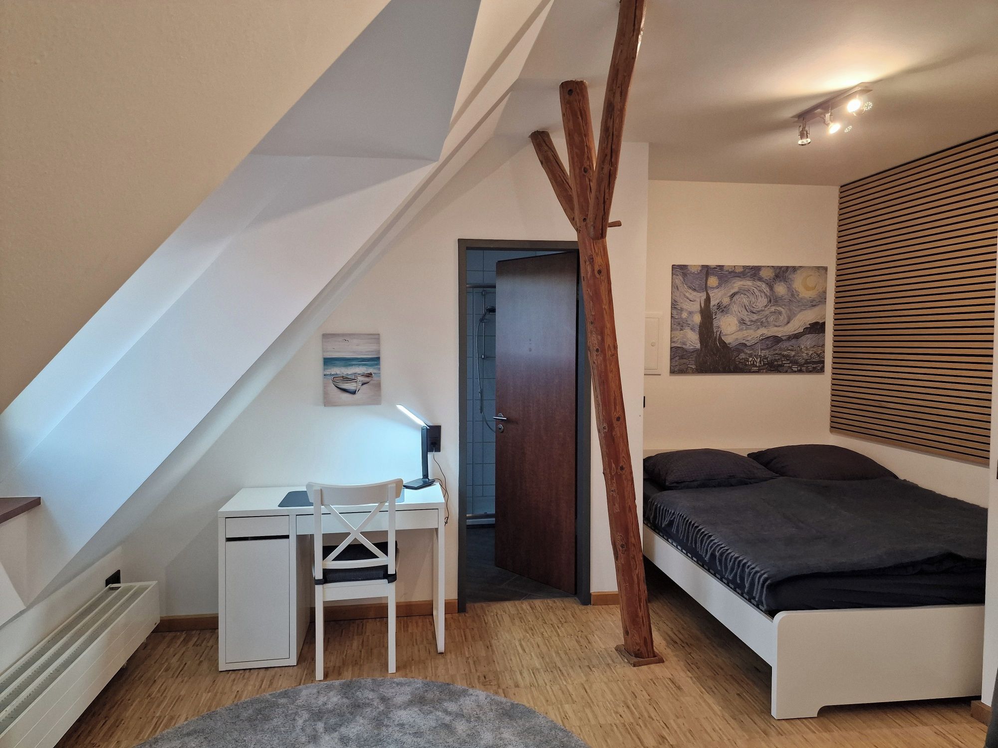 Ein Schlafzimmer mit geneigter Decke, einem Schreibtisch, einem Bett und einem Gemälde.