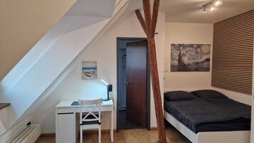 Ein Schlafzimmer mit geneigter Decke, einem Schreibtisch, einem Bett und einem Gemälde.