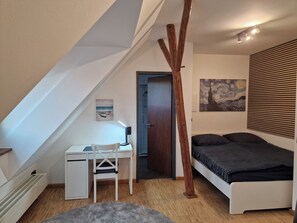 Ein Schlafzimmer mit geneigter Decke, einem Schreibtisch, einem Bett und einem Gemälde.
