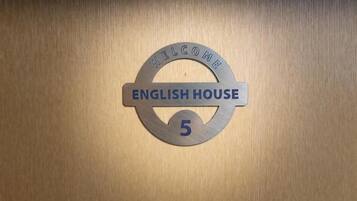 Un cartel de bienvenida con 'ENGLISH HOUSE 5' sobre una superficie de madera.