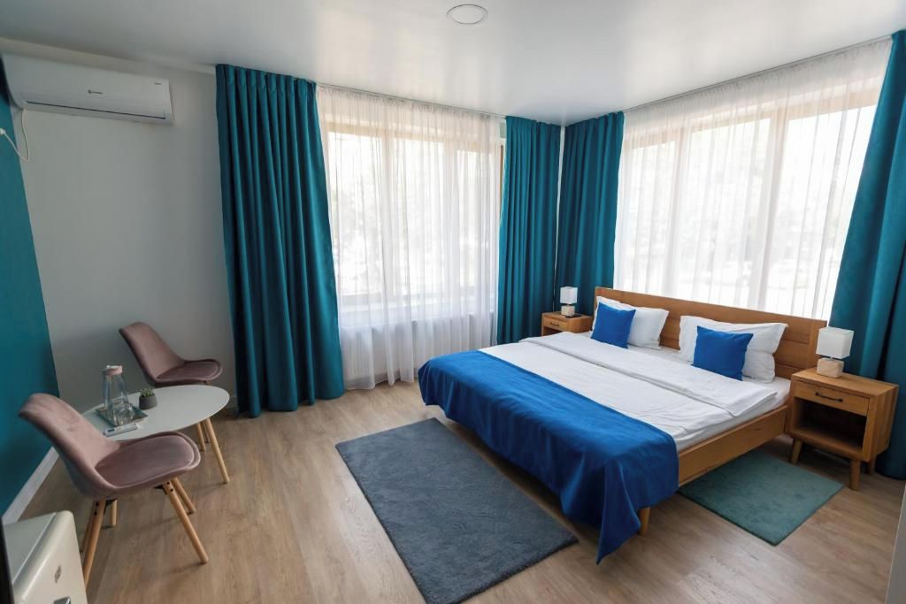Habitación de hotel con cama, mesitas de noche, escritorio y sillas, y ventana con cortinas.