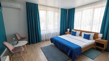 Habitación de hotel con cama, mesitas de noche, escritorio y sillas, y ventana con cortinas.