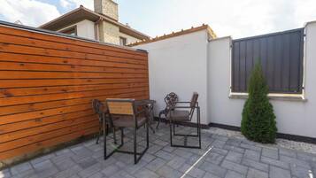 A patio with two metal-framed chairs and a table, a wooden fence, and a small coniferous tree.