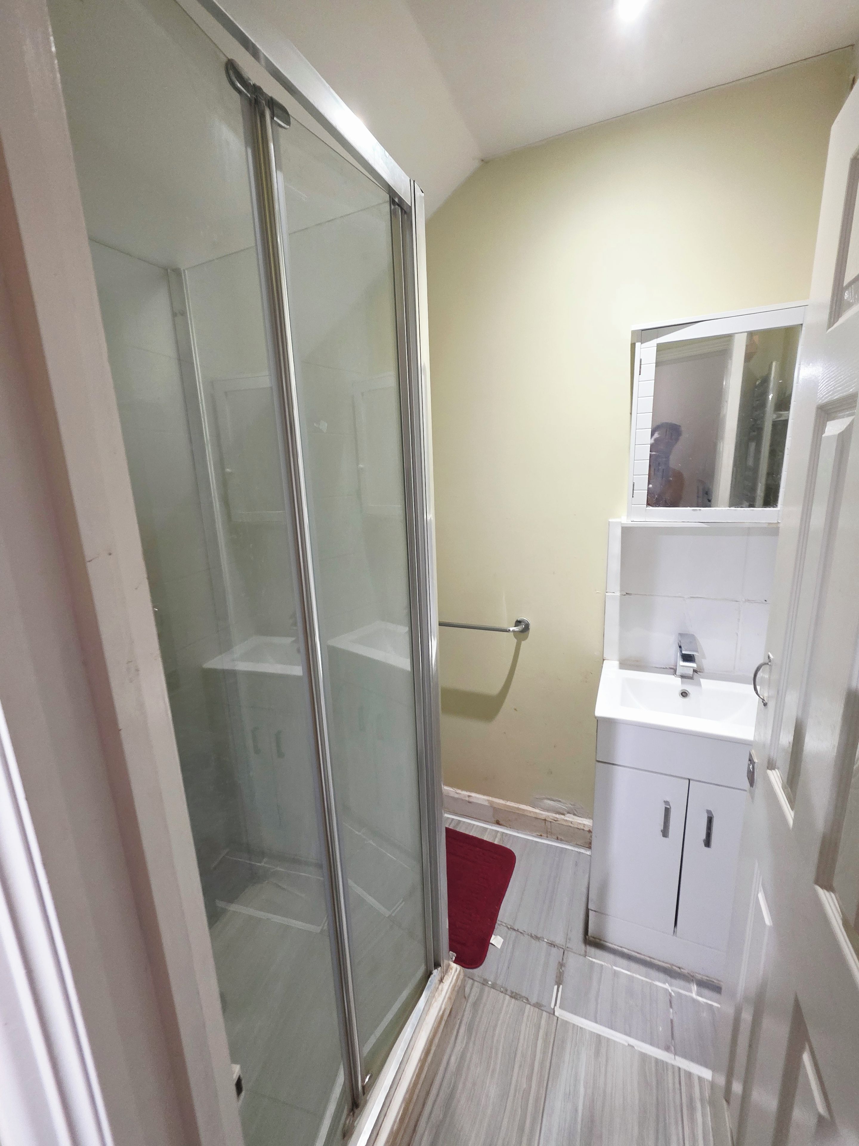 A bathroom with a glass shower enclosure, a white sink, and a mirror above it.