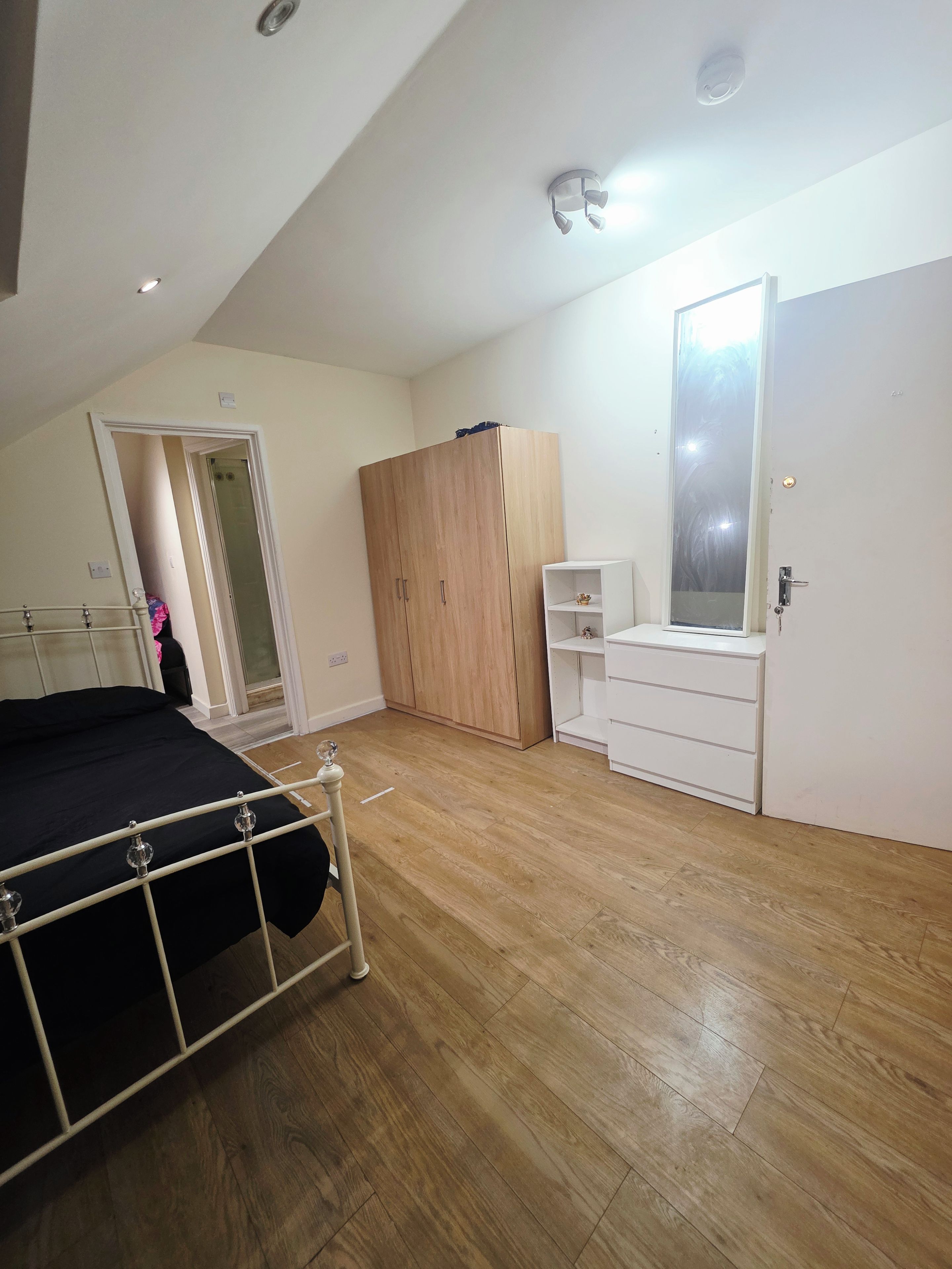 A bedroom with a bed, wardrobe, dresser, and a door with a mirror.