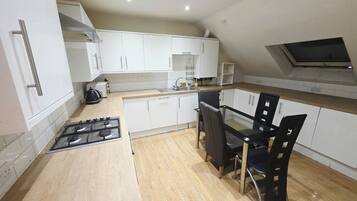 A modern kitchen with white cabinets, a gas stove, a dining table with chairs, and a skylight.