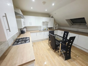 A modern kitchen with white cabinets, a gas stove, a dining table with chairs, and a skylight. - Heathrow Tranquil 4-bedroom apartment in delightful Feltham perfect for families (Feltham)