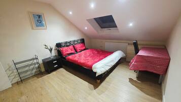 A bedroom with a bed, bedside table, and a small table with a red tablecloth.
