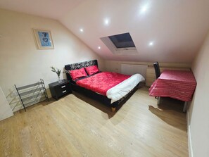 A bedroom with a bed, bedside table, and a small table with a red tablecloth. - Heathrow Tranquil 4-bedroom apartment in delightful Feltham perfect for families (Feltham)