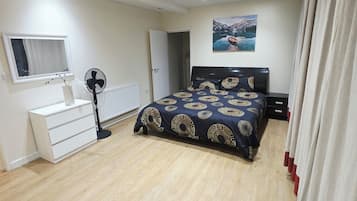 A bedroom with a bed, a dresser, a fan, a window, and a painting on the wall.