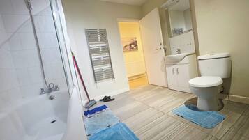 A bathroom with a bathtub, a toilet, a showerhead, a towel rack, and a mirror.