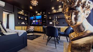 Una sala de estar moderna con un sofá, una mesa de centro y un televisor. Hay objetos decorativos en estantes y una estatua sobre un pedestal.