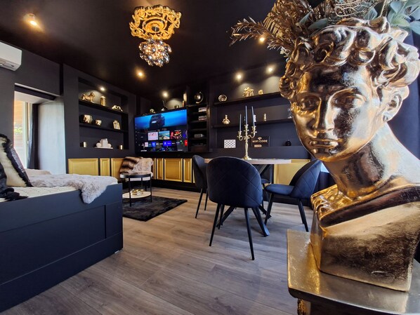 A modern living room with a sofa, a coffee table, and a TV. There are decorative items on shelves and a statue on a pedestal.