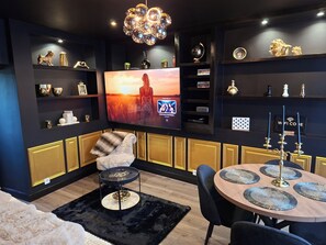 A modern living room with a flat-screen TV, a cozy seating area, and a decorative chandelier.