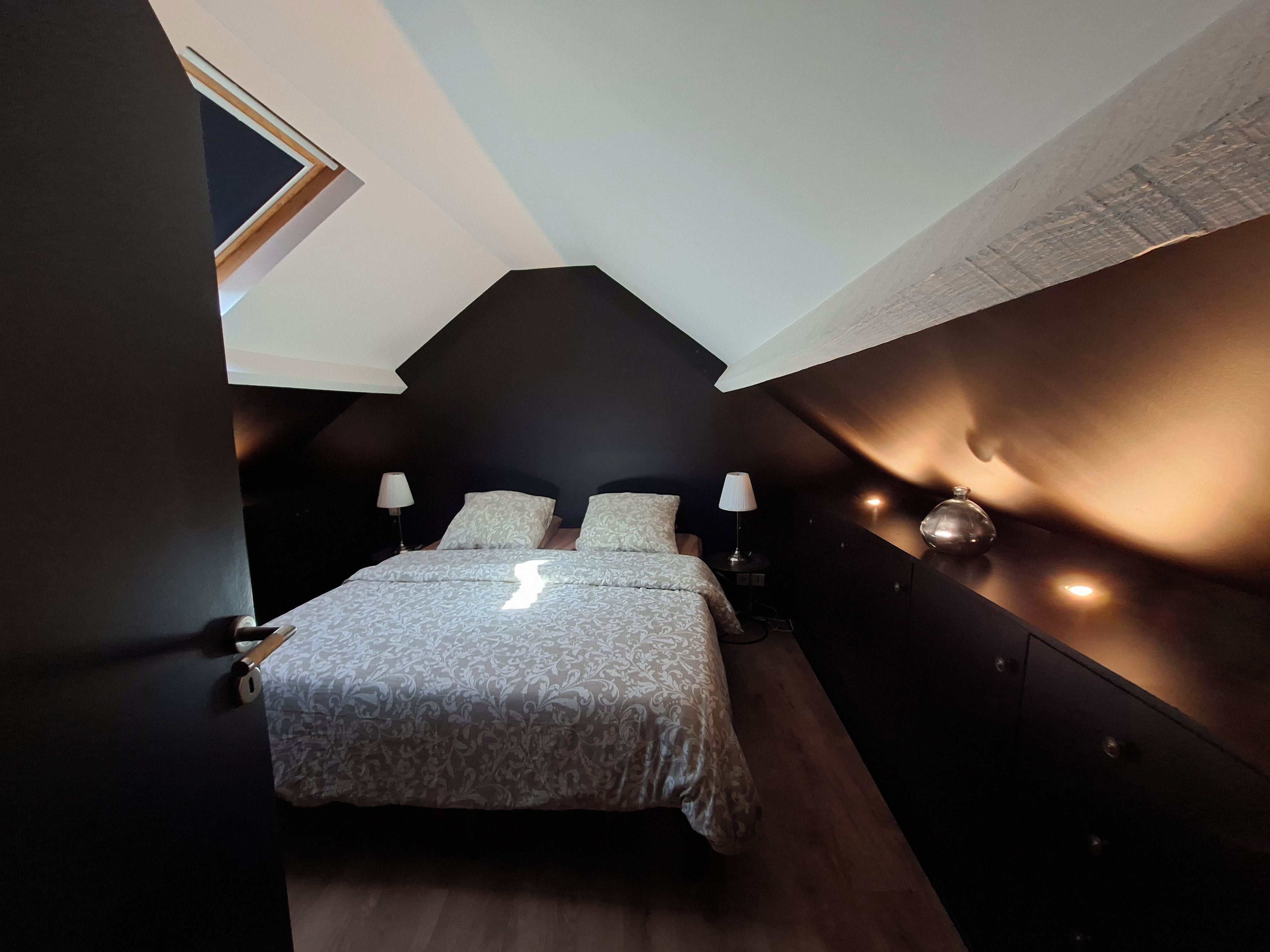 Et soveværelse med en seng, to sengeborde med lamper, et lille bord og en lampe på væggen.